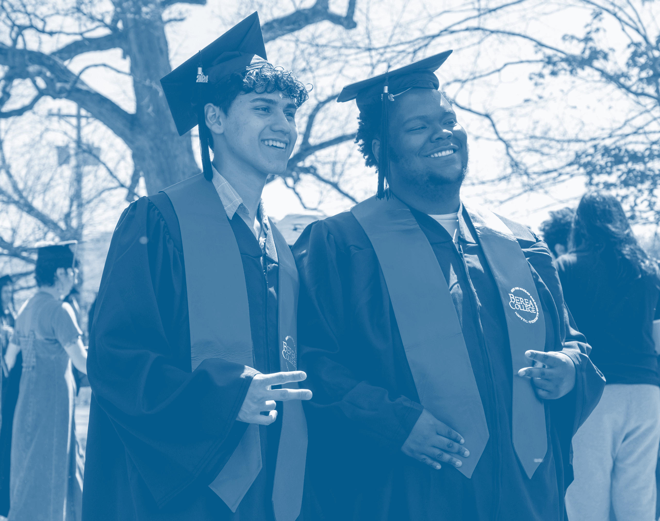 Two students in caps and gowns smiling at a graduation ceremony with a blue filter