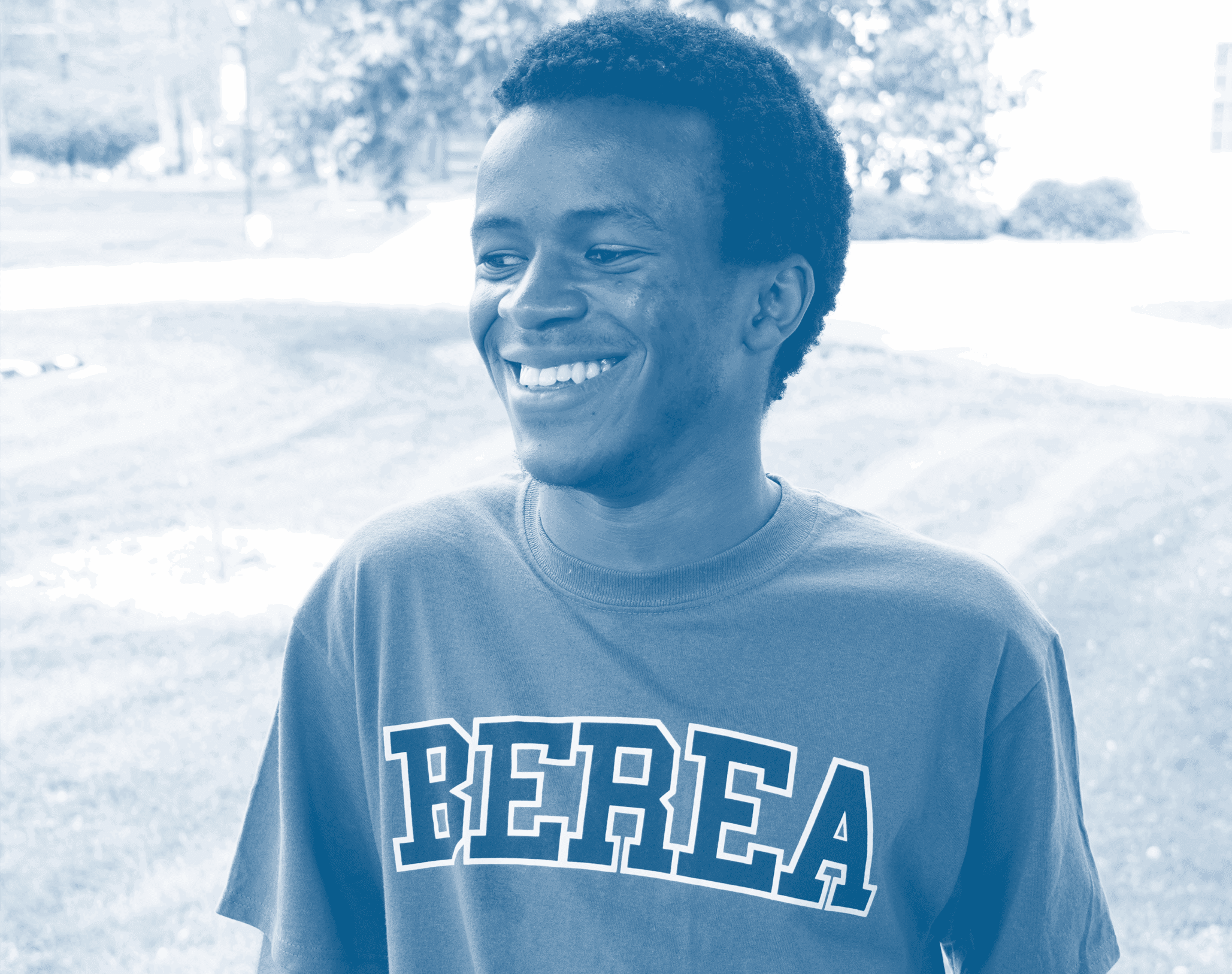 A student leaning against a porch railing, looking away from the camera, smiling, in a shirt that says 'Berea'. The photo has a blue filter over it.