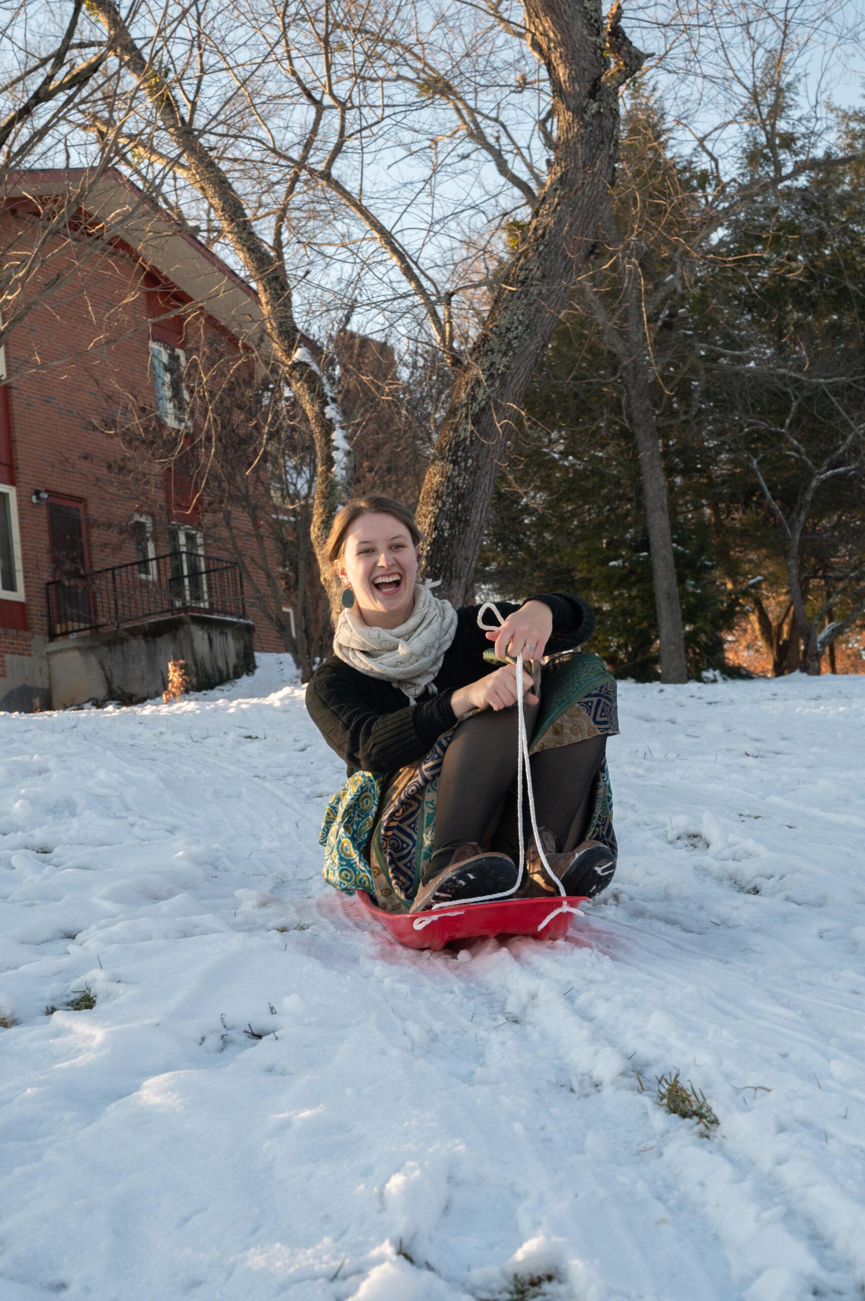 A student sledding down a hill, covered in snow.